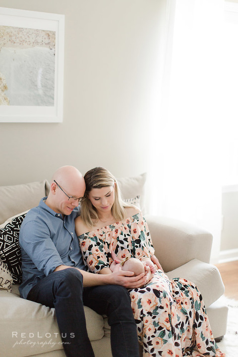 in home newborn photographer parents holding baby on sofa looking down smiling