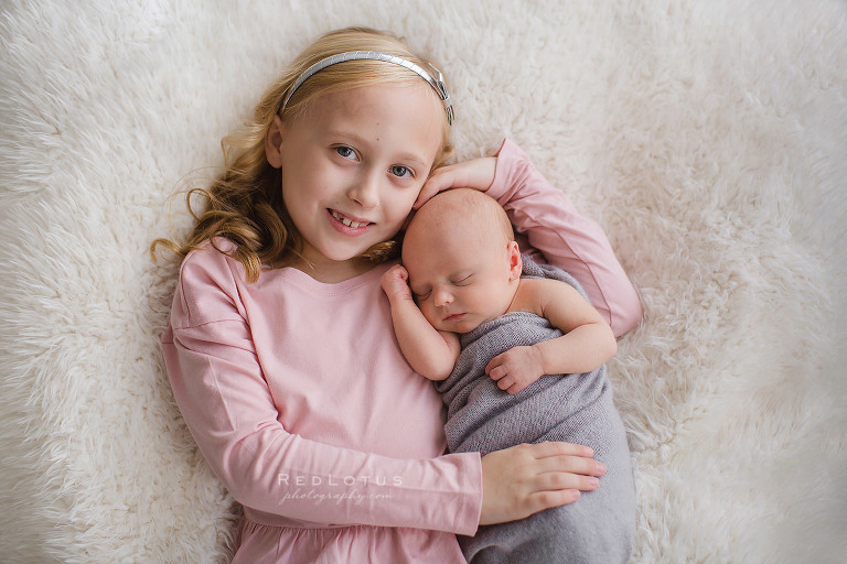 girl and newborn sister sibling newborn pose laying on furry blanket