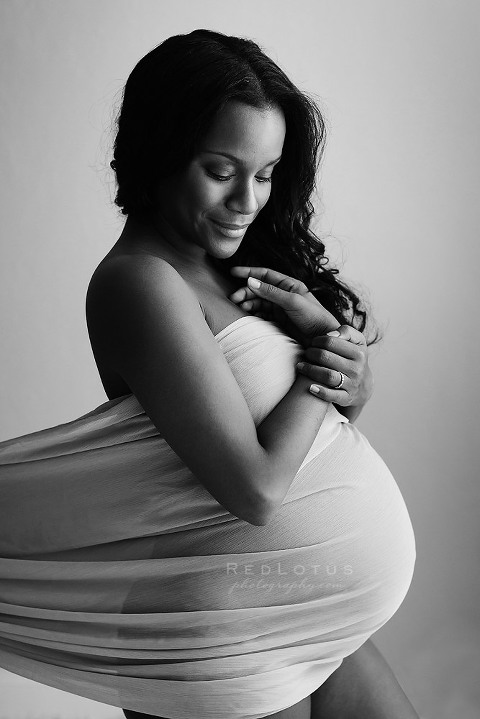black and white pregnancy photo of a woman wrapped in sheer fabric