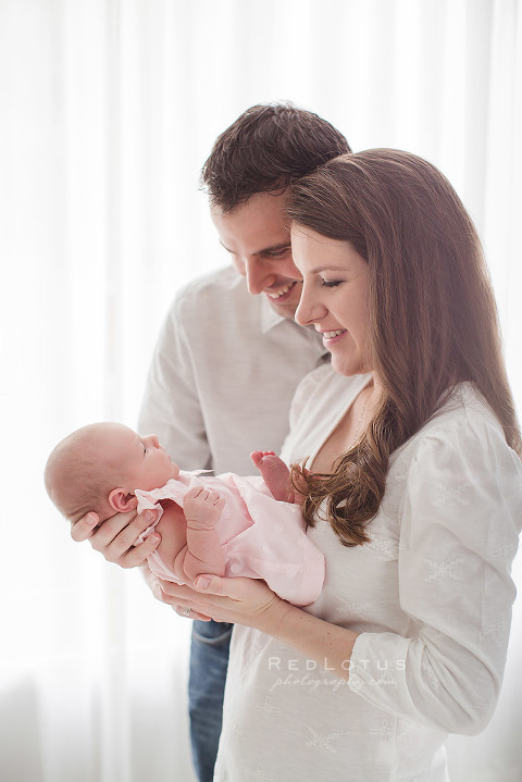 newborn photography parent and baby pose neutral backdrop natural window light mom and dad looking at baby