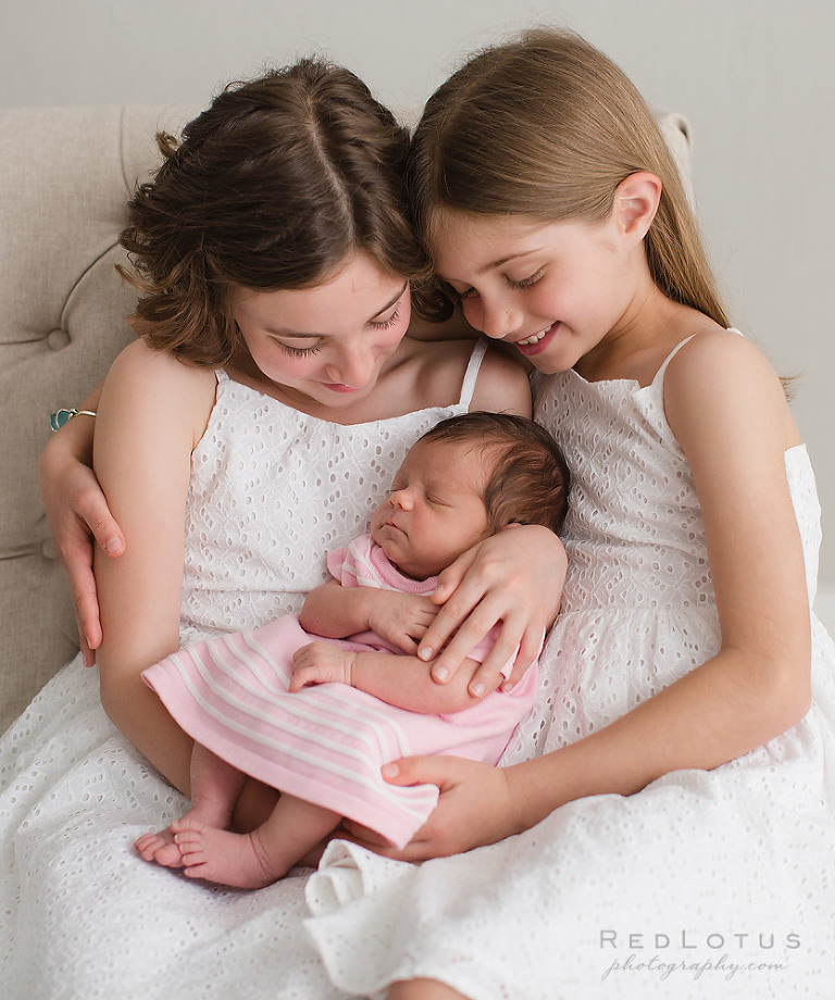 newborn baby girl held by sibling sisters newborn portrait photography