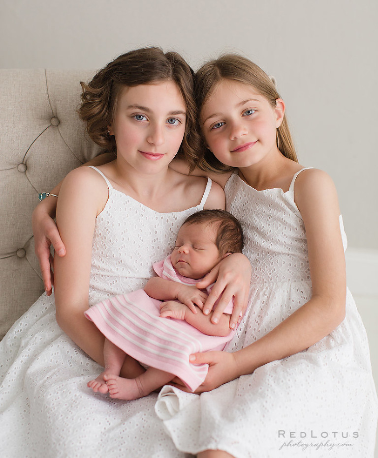 newborn pose with siblings baby with older sisters