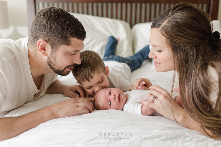 newborn photography family on bed looking at baby