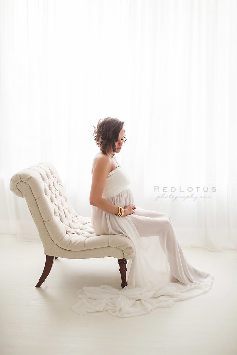 classic maternity photography woman sitting on a chair holding belly maternity dress natural light studio neutral color palette