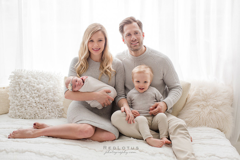 newborn family pose sitting on bed light and airy studio