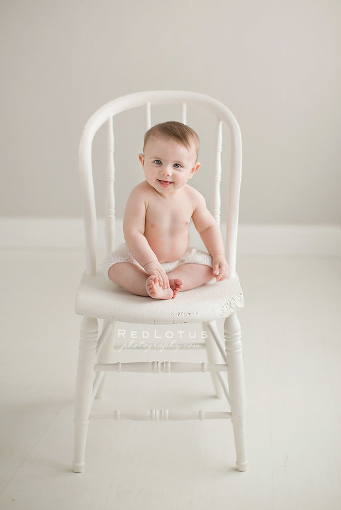 6 month old baby smiling sitting on a chair pose neutral colors white grey airy classic portrait