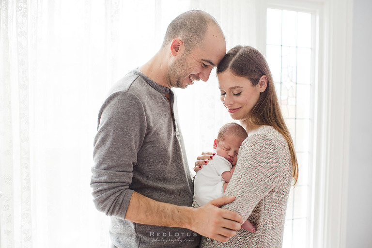home newborn photo session light airy newborn photography backlit window parents and baby pose near window