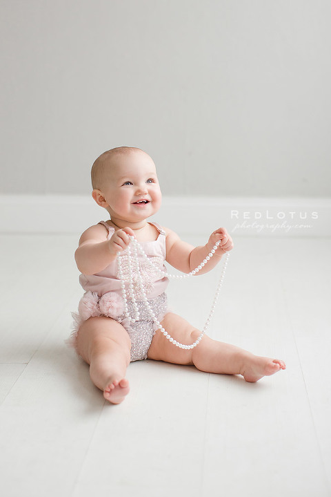 one year photo session baby girl playing with string of pearls