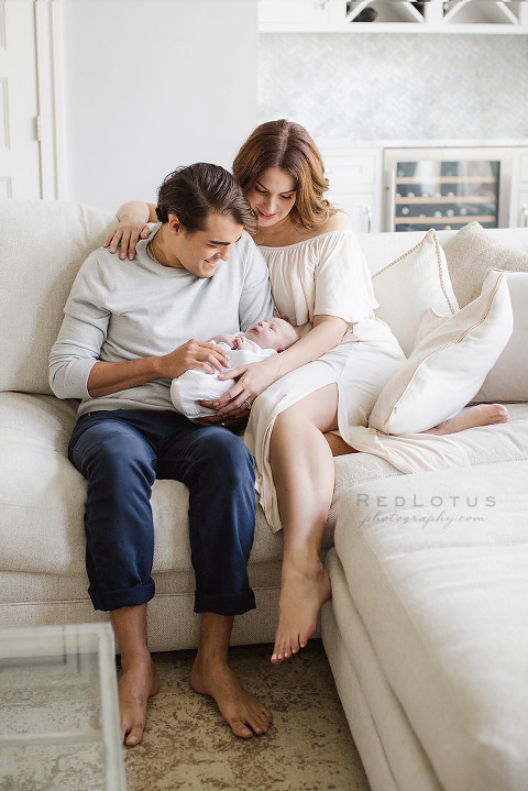 parents holding baby smiling sitting on couch light and airy neutral natural light home newborn session