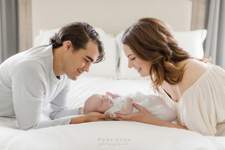 lifestlye newborn session pose mom and dad smiling at baby on bed