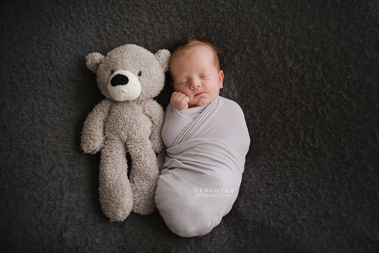 newborn baby sleeping next to teddy bear