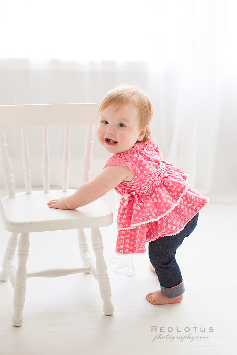one year old girl toddler pink dress standing with chair white studio