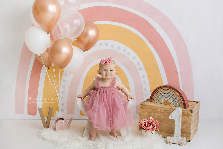 first birthday photo session girl with a boho rainbow backdrop colors of dusty rose and gold