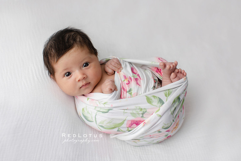 newborn baby girl with floral wrap and white backdrop