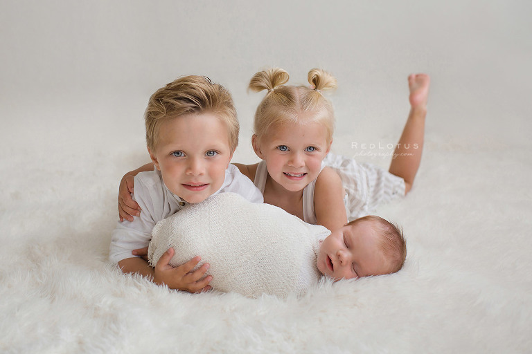 newborn and siblings laying on floor white backdrop neutral