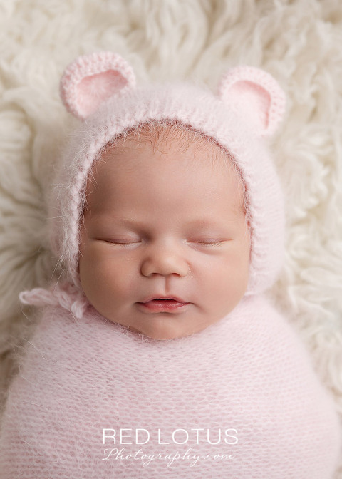 newborn girl in a pink wrap and pink teddy bear hat