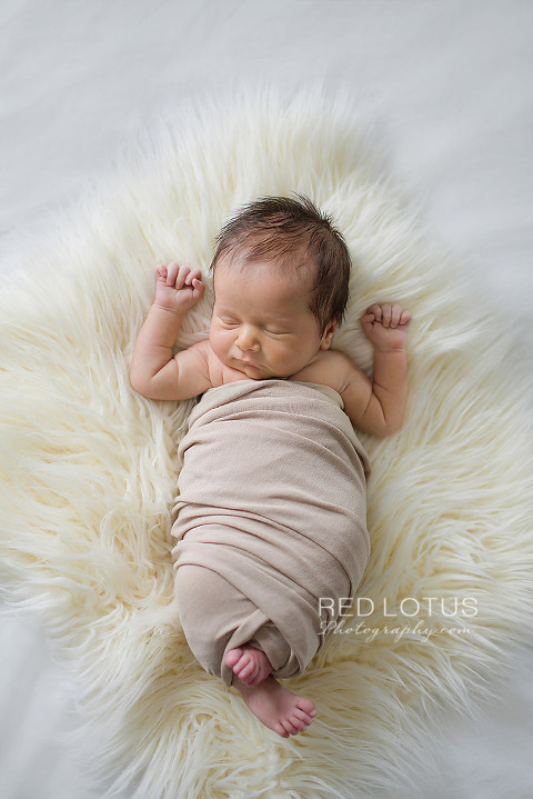 home newborn session baby wrapped in neutral color sleeping on the bed