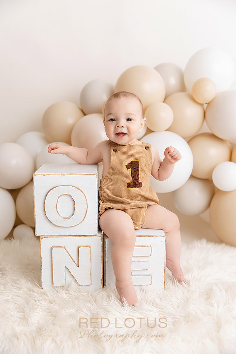 one year old baby boy sitting on blocks with a neutral balloon garland backdrop