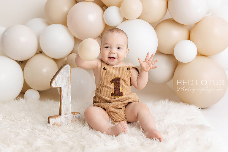one year old baby boy with a neutral balloon garland backdrop