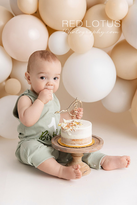 one year old baby boy with a neutral balloon garland backdrop