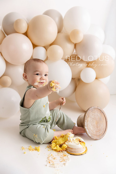 happy one year old baby boy with a neutral balloon garland backdrop