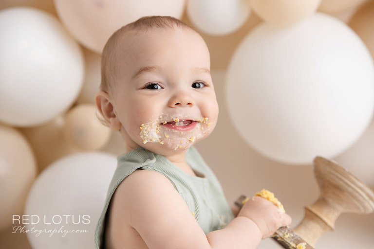 happy one year old baby boy with a neutral balloon garland backdrop
