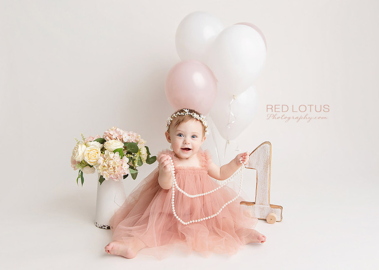 one year old toddler girl wearing pink blush tulle with balloons and flowers golding string of pearls