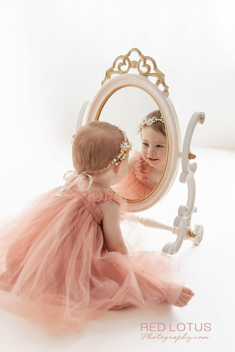 one year old toddler girl smiling at her reflection in the mirror