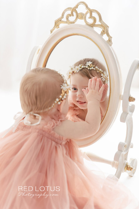 one year old toddler girl smiling at her reflection in the mirror