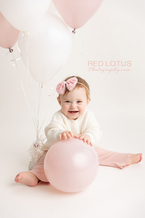 one year old toddler girl holding blush pink balloon and smiling
