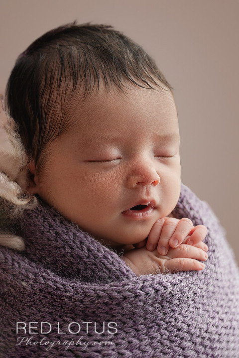 newborn baby in purple swaddle wrap sleeping