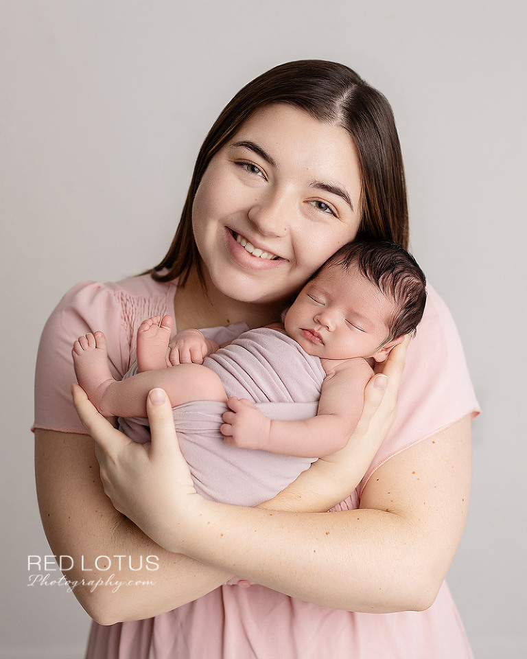 mother in pink dress holding newborn baby girl in her arms