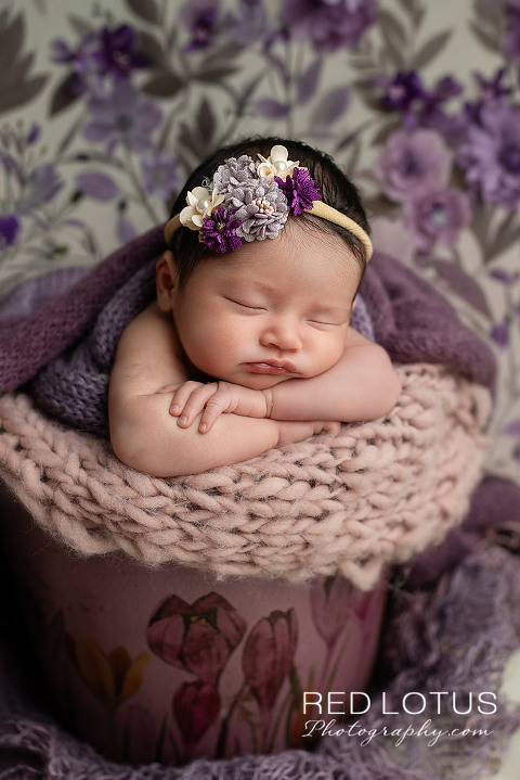 newborn baby girl posed in a purple bucket with flowers