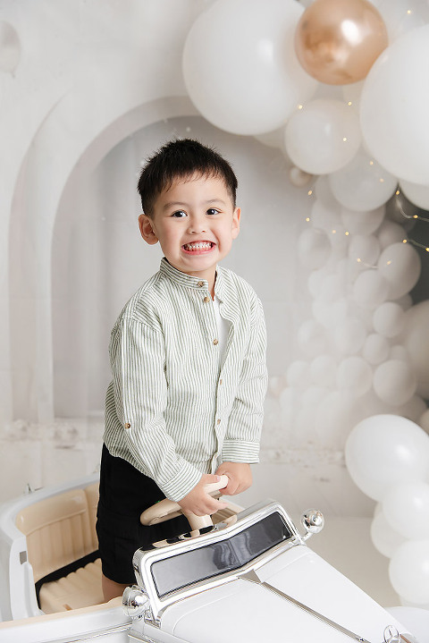 three year old boy standing and smiling in his toy car