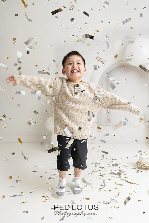three year old boy jumps for joy with confetti falling