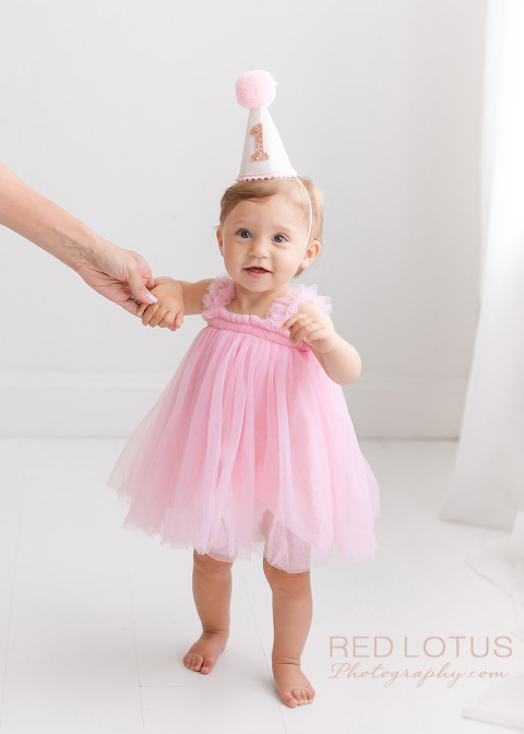 one year old girl photo session girl in pink dress and party hat holding mother's hand