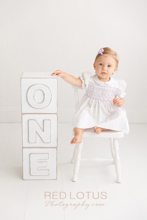 one year old girl photo session girl wearing a white dress and sitting in a chair next to blocks that spell one