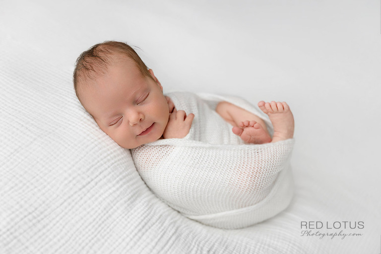 newborn baby girl wrapped in neutral white swaddle smiling