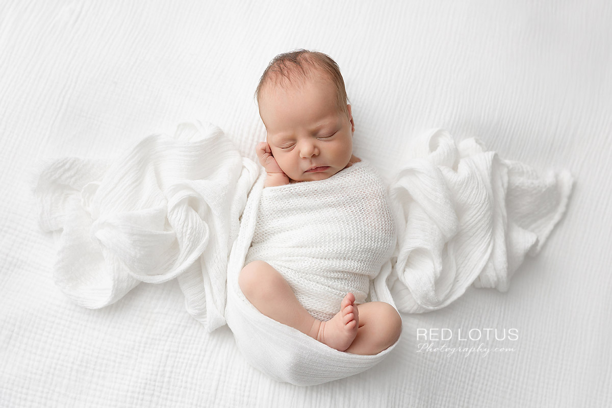 newborn baby girl wrapped in neutral white swaddle