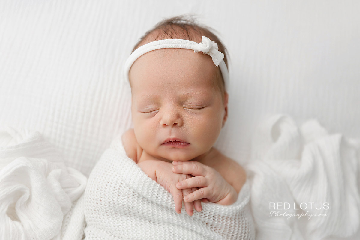newborn baby girl wrapped in neutral white swaddle