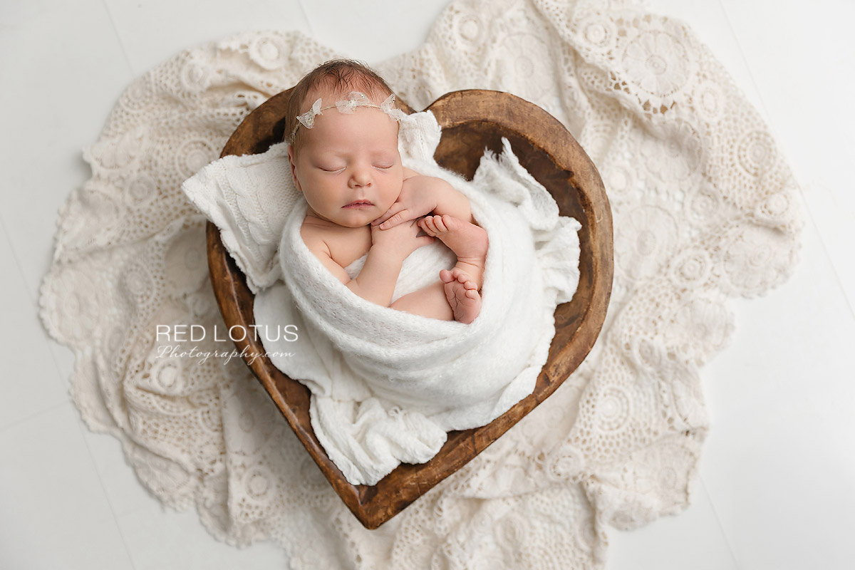 newborn baby wrapped in neutral white swaddle sleeping in wooden hear prop