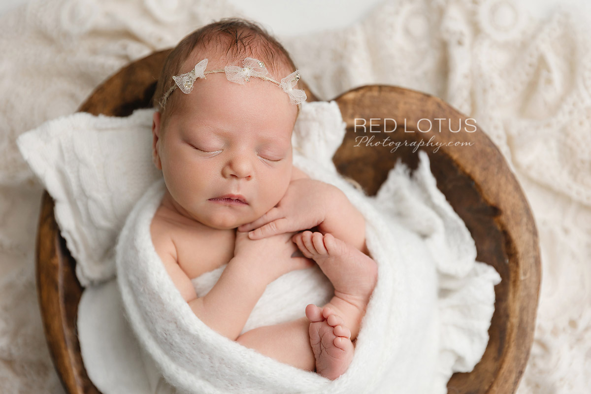 newborn baby wrapped in neutral white swaddle sleeping in wooden hear prop