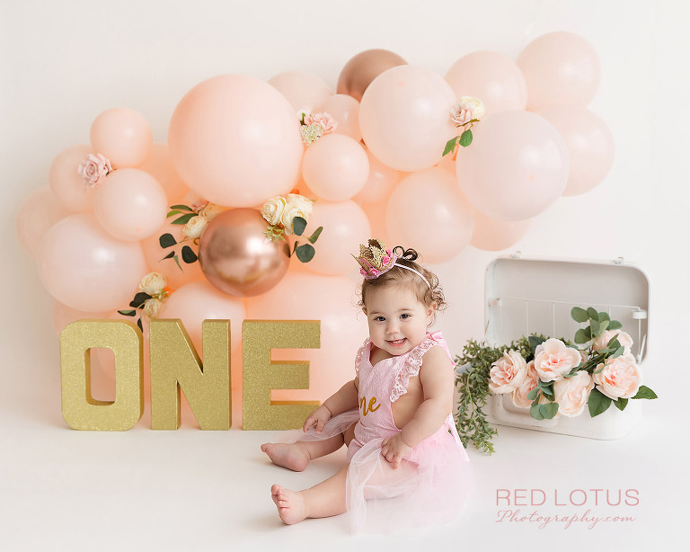 first birthday photo session toddler girl with peach colored balloon garland and roses