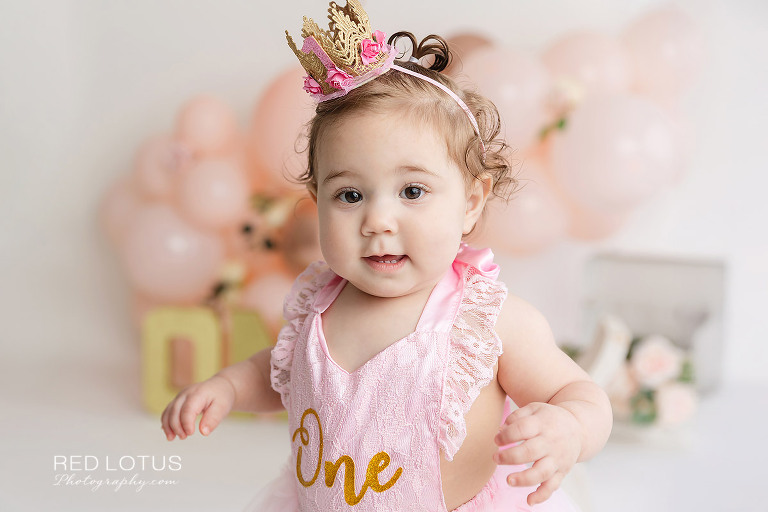 first birthday photo session toddler girl with peach colored balloon garland and roses