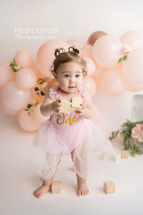 first birthday photo session toddler girl with peach colored balloon garland and roses