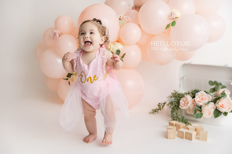 first birthday photo session toddler girl with peach colored balloon garland and roses
