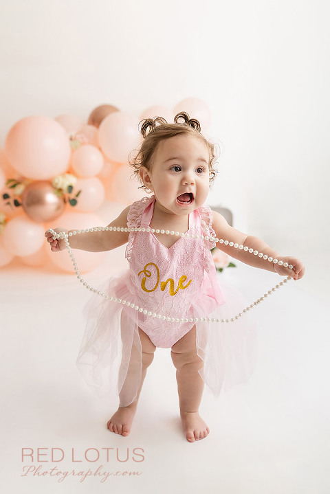 first birthday photo session toddler girl with peach colored balloon garland and roses
