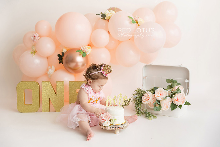 first birthday photo session toddler girl with peach colored balloon garland and roses