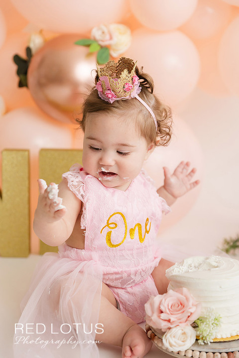 first birthday photo session toddler girl with peach colored balloon garland and roses